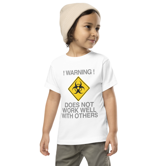 "!Warning! Does Not Work Well With Others" printed on a white toddler short sleeve tee worn by a male wearing a cap