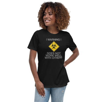 "!Warning! Does Not Work Well With Others" printed on a black women's relaxed t-shirt worn by a female