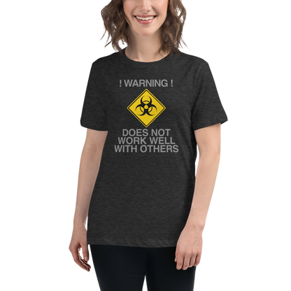 "!Warning! Does Not Work Well With Others" printed on a dark grey heather women's relaxed t-shirt worn by a female