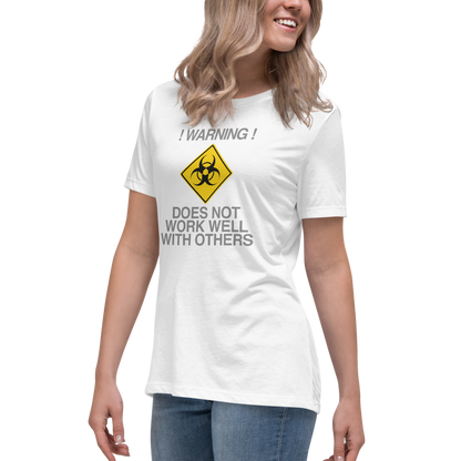 "!Warning! Does Not Work Well With Others" printed on a white women's relaxed t-shirt worn by a female