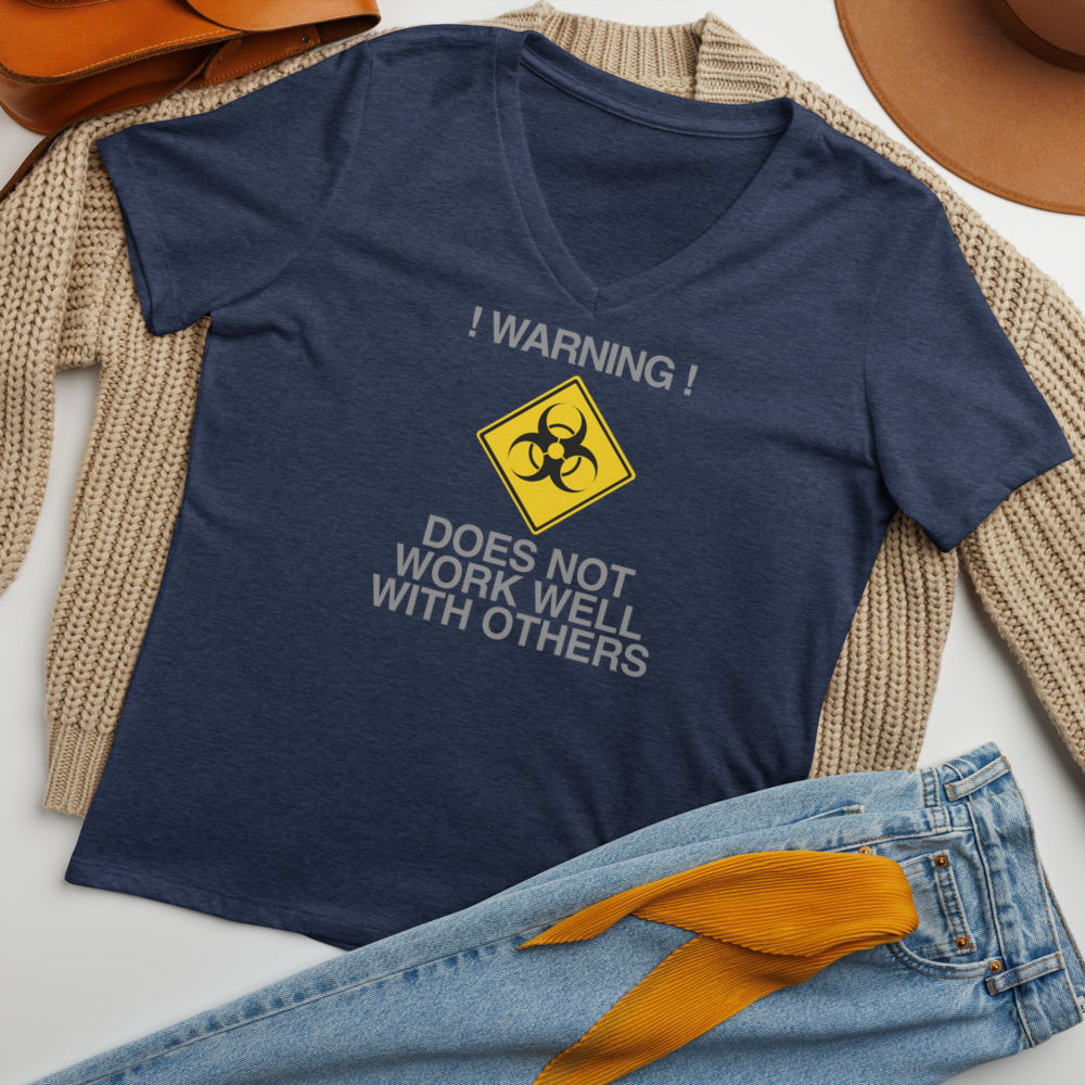 "!Warning! Does Not Work Well With Others" printed on a heather navy women's relaxed v-neck t-shirt laying on a flat surface amongst other clothes