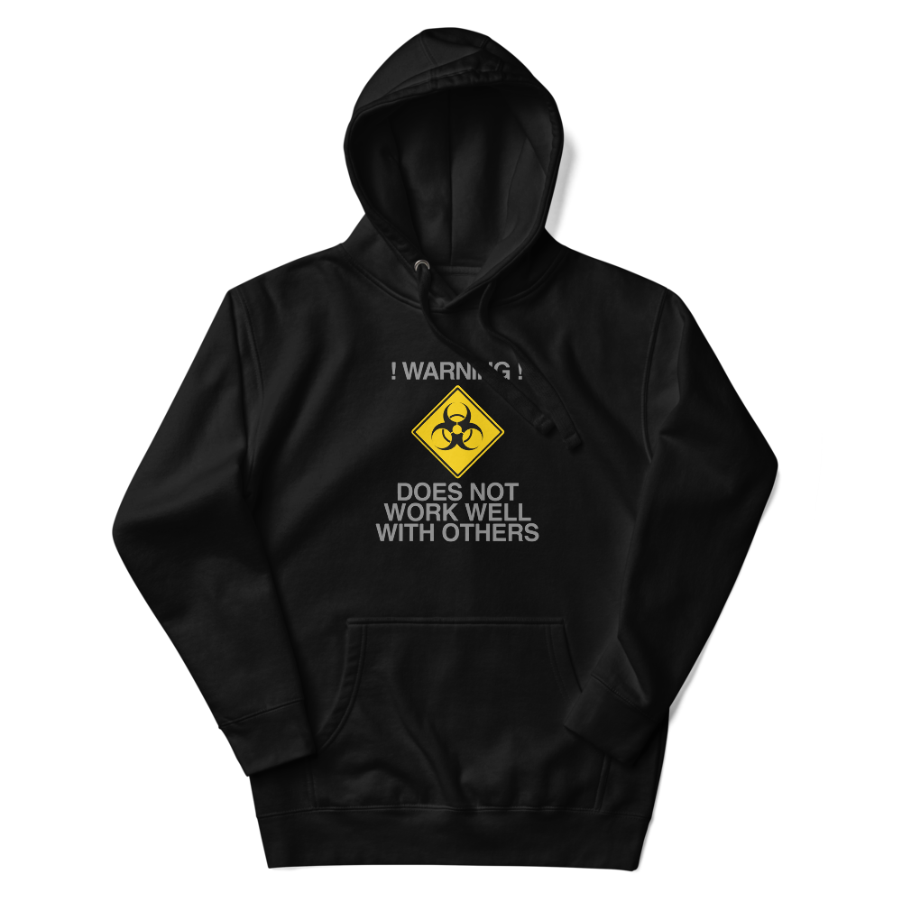 "!Warning! Does Not Work Well With Others" printed on a black unisex hoodie laying on a flat surface with the hood up