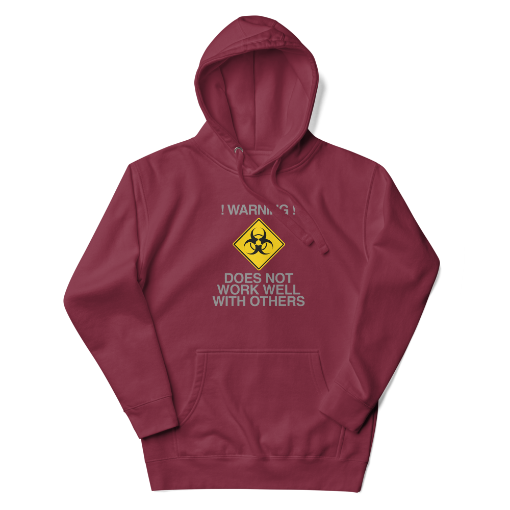 "!Warning! Does Not Work Well With Others" printed on a maroon unisex hoodie laying on a flat surface with the hood up