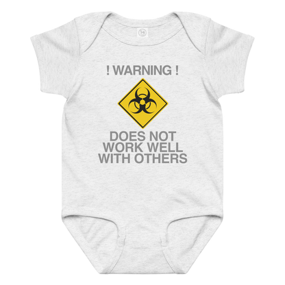 "!Warning! Does Not Work Well With Others" printed on a ash baby jersey bodysuit laying on a flat surface amongst other clothes
