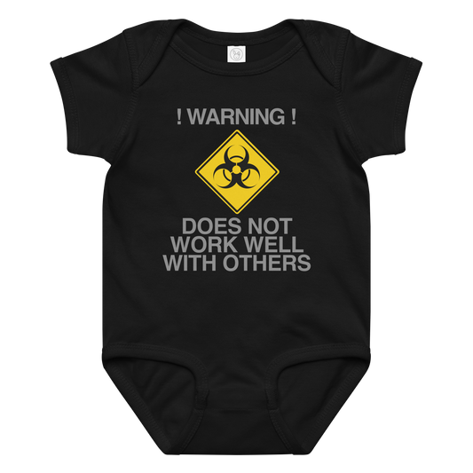 "!Warning! Does Not Work Well With Others" printed on a black baby jersey bodysuit laying on a flat surface amongst other clothes