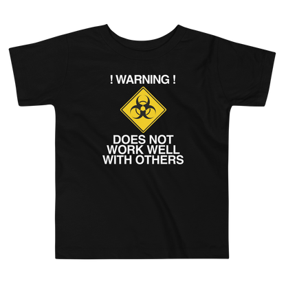 "!Warning! Does Not Work Well With Others" printed on a black toddler short sleeve tee laying on a flat surface