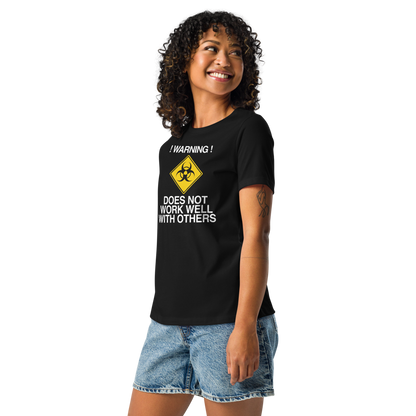 "!Warning! Does Not Work Well With Others" printed on a black women's relaxed t-shirt worn by a female