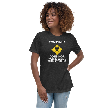 "!Warning! Does Not Work Well With Others" printed on a dark grey heather women's relaxed t-shirt worn by a female
