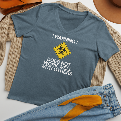 "!Warning! Does Not Work Well With Others" printed on a heather slate women's relaxed v-neck t-shirt laying on a flat surface amongst other clothes