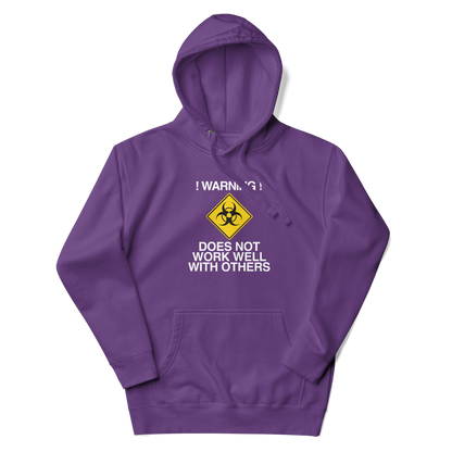 "!Warning! Does Not Work Well With Others" printed on a purple unisex hoodie laying on a flat surface with the hood up
