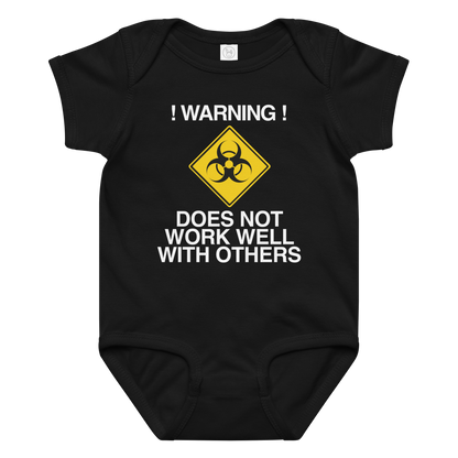 "!Warning! Does Not Work Well With Others" printed on a black baby jersey bodysuit laying on a flat surface amongst other clothes