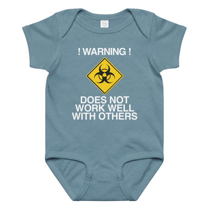 "!Warning! Does Not Work Well With Others" printed on a vintage indigo baby jersey bodysuit laying on a flat surface amongst other clothes