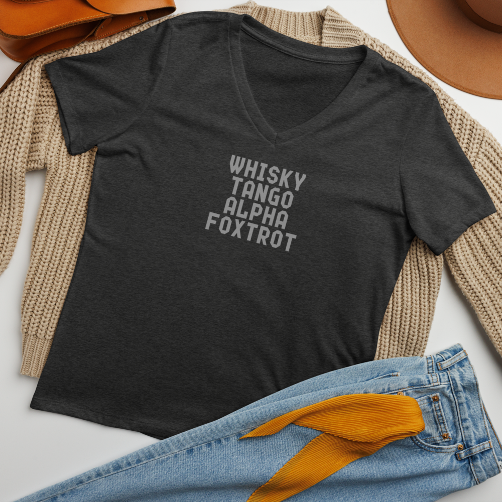 "Whisky Tango Alpha Foxtrot" printed on a dark grey heather women's relaxed v-neck t-shirt laying on a flat surface amongst other clothes