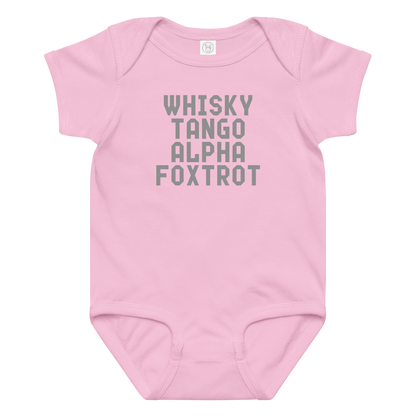 "Whisky Tango Alpha Foxtrot" printed on a pink baby jersey bodysuit laying on a flat surface amongst other clothes