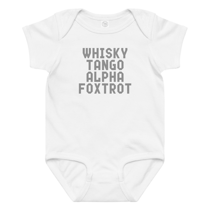 "Whisky Tango Alpha Foxtrot" printed on a white baby jersey bodysuit laying on a flat surface amongst other clothes