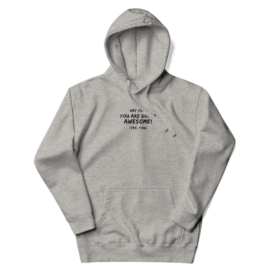 "Hey You! You are doing awesome! (Yes, you)" printed on a carbon grey unisex hoodie laying on a flat surface with the hood up