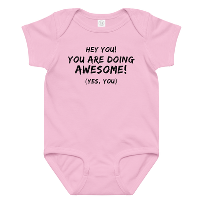 "Hey You! You are doing awesome! (Yes, you)" printed on a pink baby jersey bodysuit laying on a flat surface amongst other clothes