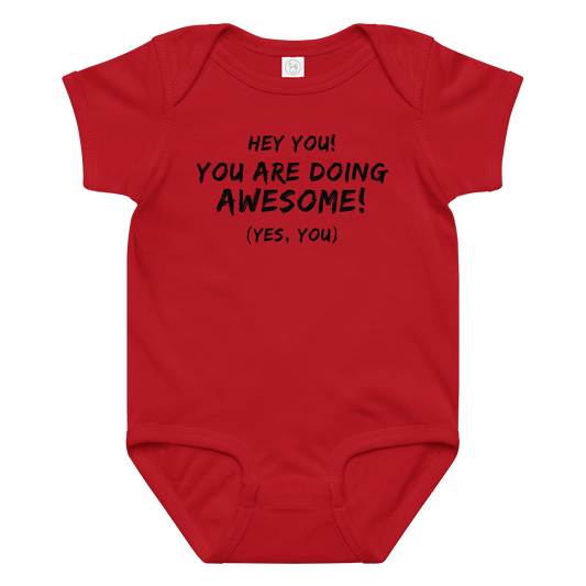 "Hey You! You are doing awesome! (Yes, you)" printed on a red baby jersey bodysuit laying on a flat surface amongst other clothes