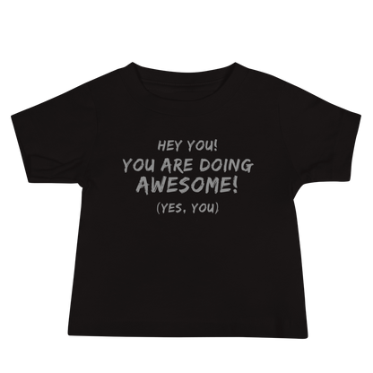 "Hey You! You are doing awesome! (Yes, you)" printed on a black baby jersey short sleeve tee laying on a flat surface