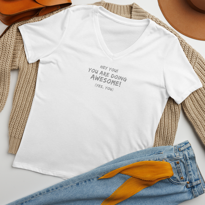 "Hey You! You are doing awesome! (Yes, you)" printed on a solid white blend women's relaxed v-neck t-shirt laying on a flat surface amongst other clothes