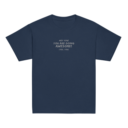 "Hey You! You are doing awesome! (Yes, you)" printed on a navy youth classic tee laying on a flat surface