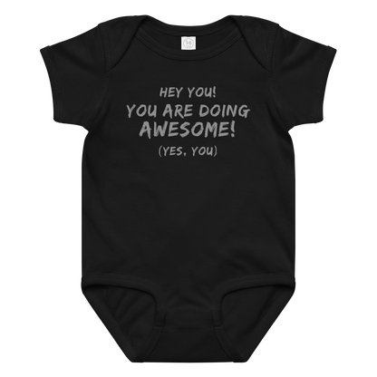 "Hey You! You are doing awesome! (Yes, you)" printed on a black baby jersey bodysuit laying on a flat surface amongst other clothes