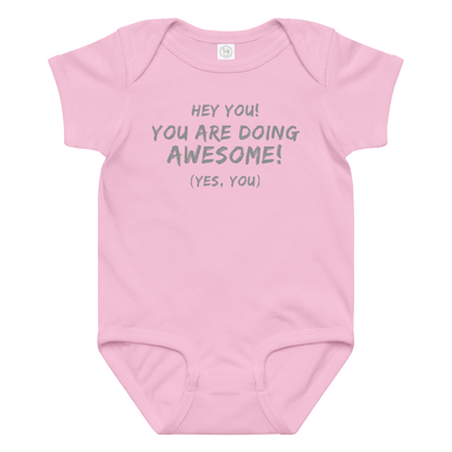 "Hey You! You are doing awesome! (Yes, you)" printed on a pink baby jersey bodysuit laying on a flat surface amongst other clothes