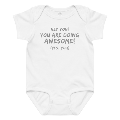 "Hey You! You are doing awesome! (Yes, you)" printed on a white baby jersey bodysuit laying on a flat surface amongst other clothes