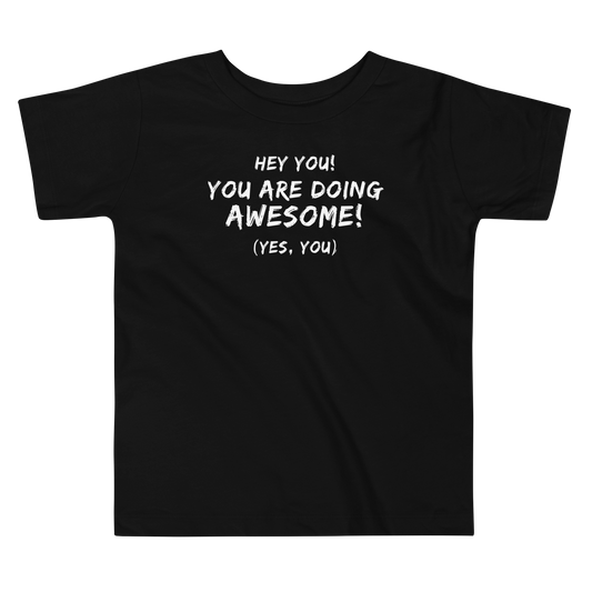 "Hey You! You are doing awesome! (Yes, you)" printed on a black toddler short sleeve tee laying on a flat surface