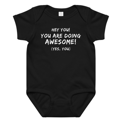 "Hey You! You are doing awesome! (Yes, you)" printed on a black baby jersey bodysuit laying on a flat surface amongst other clothes
