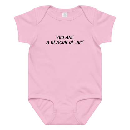 "You are a beacon of joy" printed on a pink baby jersey bodysuit laying on a flat surface amongst other clothes