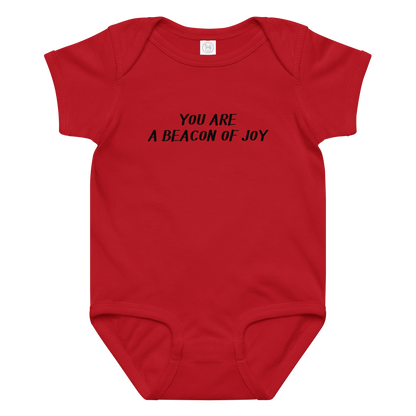 "You are a beacon of joy" printed on a red baby jersey bodysuit laying on a flat surface amongst other clothes
