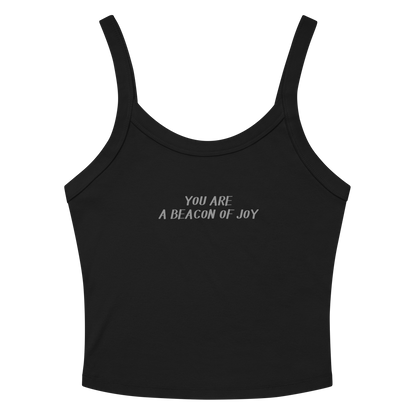 "You are a beacon of joy" printed on a solid black blend women's micro-rib tanktop laying on a flat surface amongst sunglasses and shorts