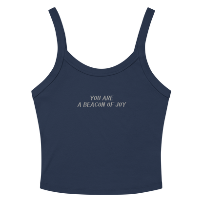 "You are a beacon of joy" printed on a solid navy blend women's micro-rib tanktop laying on a flat surface amongst sunglasses and shorts