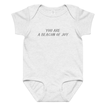 "You are a beacon of joy" printed on a ash baby jersey bodysuit laying on a flat surface amongst other clothes