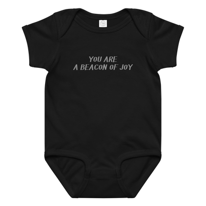 "You are a beacon of joy" printed on a black baby jersey bodysuit laying on a flat surface amongst other clothes