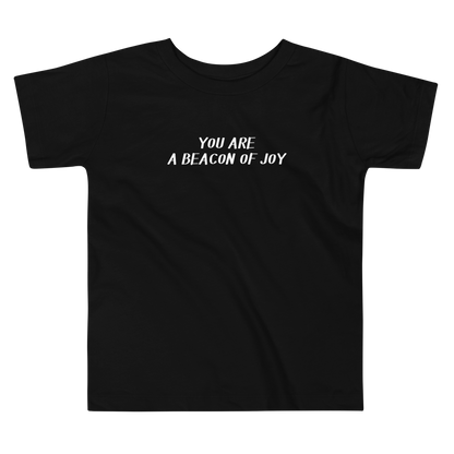 "You are a beacon of joy" printed on a black toddler short sleeve tee laying on a flat surface