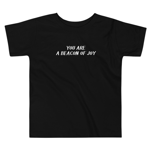 "You are a beacon of joy" printed on a black toddler short sleeve tee laying on a flat surface