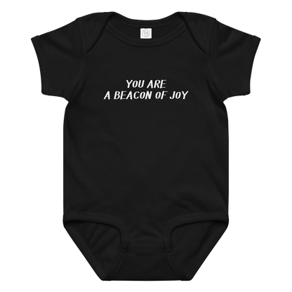 "You are a beacon of joy" printed on a black baby jersey bodysuit laying on a flat surface amongst other clothes