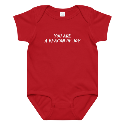 "You are a beacon of joy" printed on a red baby jersey bodysuit laying on a flat surface amongst other clothes