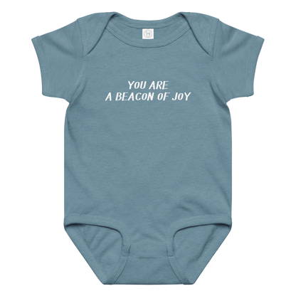 "You are a beacon of joy" printed on a vintage indigo baby jersey bodysuit laying on a flat surface amongst other clothes