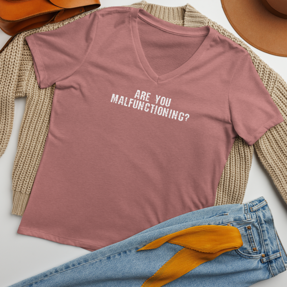 "Are you malfunctioning?" printed on a heather mauve women's relaxed v-neck t-shirt laying on a flat surface amongst other clothes