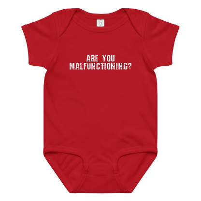 "Are you malfunctioning?" printed on a red baby jersey bodysuit laying on a flat surface amongst other clothes