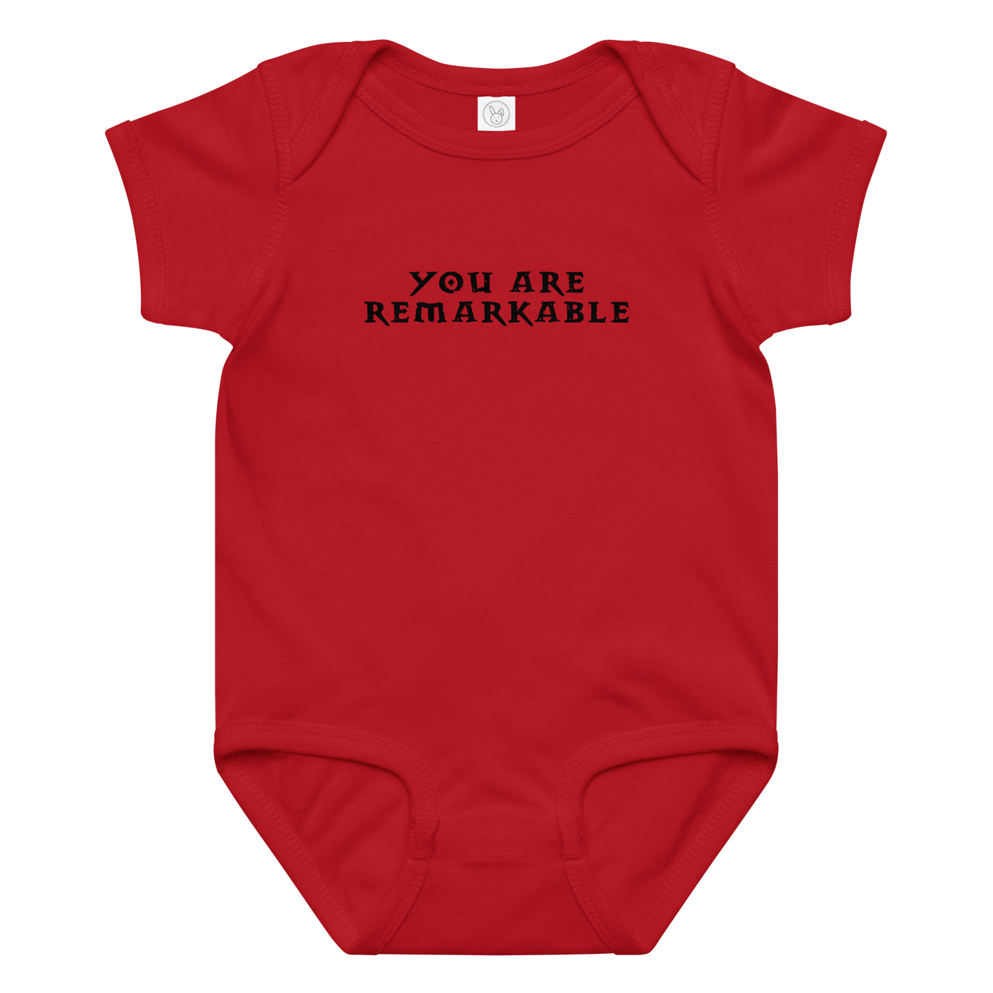 "You are remarkable" printed on a red baby jersey bodysuit laying on a flat surface amongst other clothes