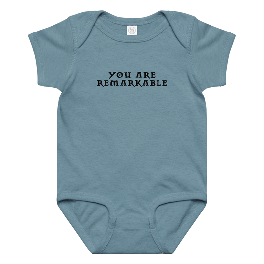 "You are remarkable" printed on a vintage indigo baby jersey bodysuit laying on a flat surface amongst other clothes