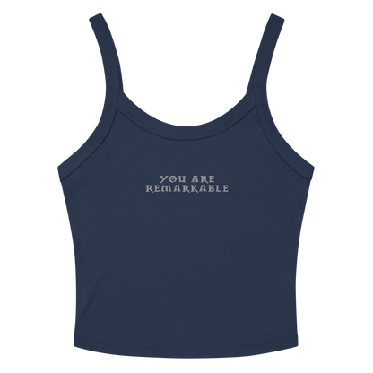 "You are remarkable" printed on a solid navy blend women's micro-rib tanktop laying on a flat surface amongst sunglasses and shorts