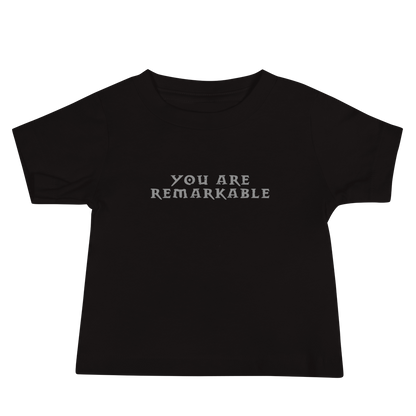 "You are remarkable" printed on a black baby jersey short sleeve tee laying on a flat surface