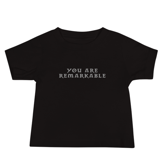 "You are remarkable" printed on a black baby jersey short sleeve tee laying on a flat surface