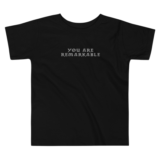 "You are remarkable" printed on a black toddler short sleeve tee laying on a flat surface