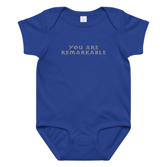 "You are remarkable" printed on a royal baby jersey bodysuit laying on a flat surface amongst other clothes